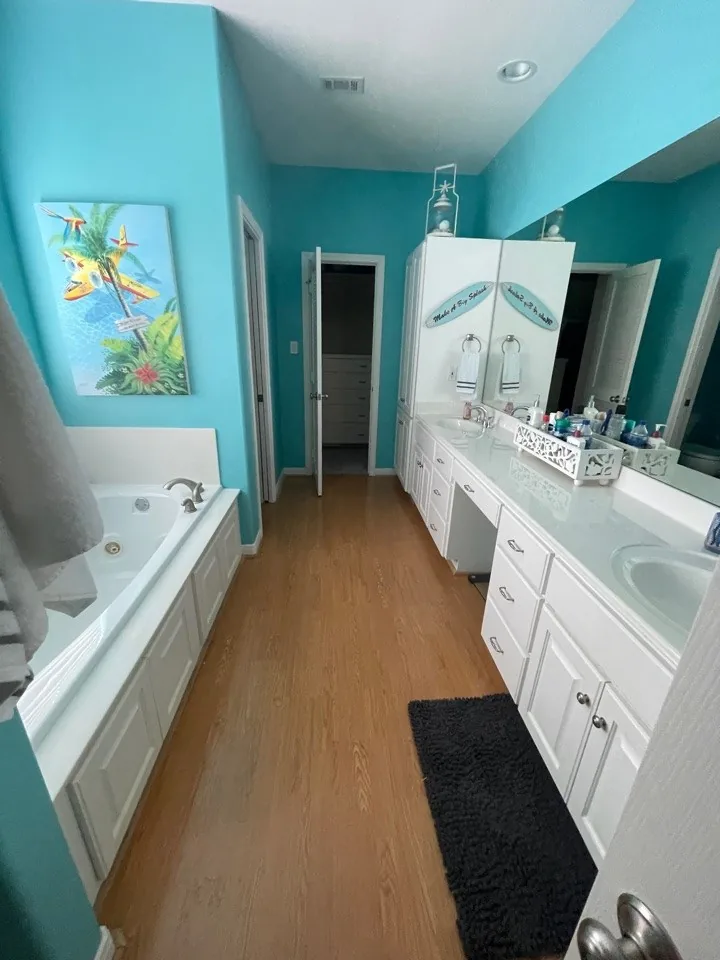Before: original primary bath in teal with a long white vanity, corner tub, and oak flooring