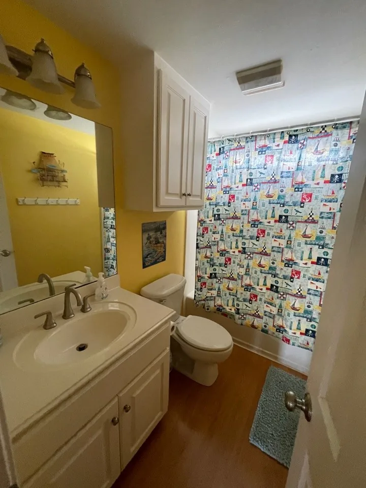 Before: original bath in yellow with a laminate vanity, curtain shower, and patterned shower curtain