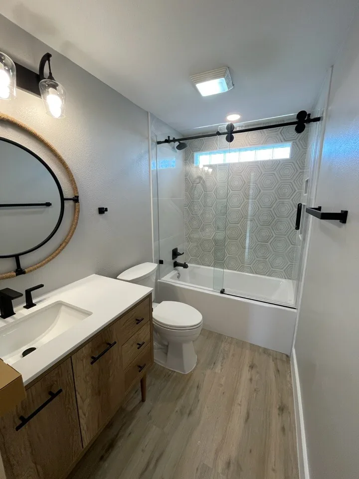 After: renovated tub bath at Tern with a wood vanity, round black mirror, and tiled tub surround