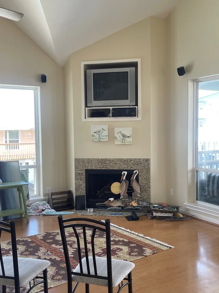 Before: original living area with a tile-surround fireplace, wall-mounted television, and dated seating