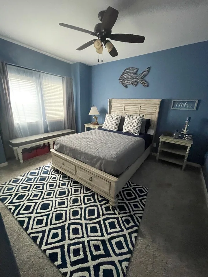 Before: original primary bedroom with navy accent wall, carpet, and a patterned area rug