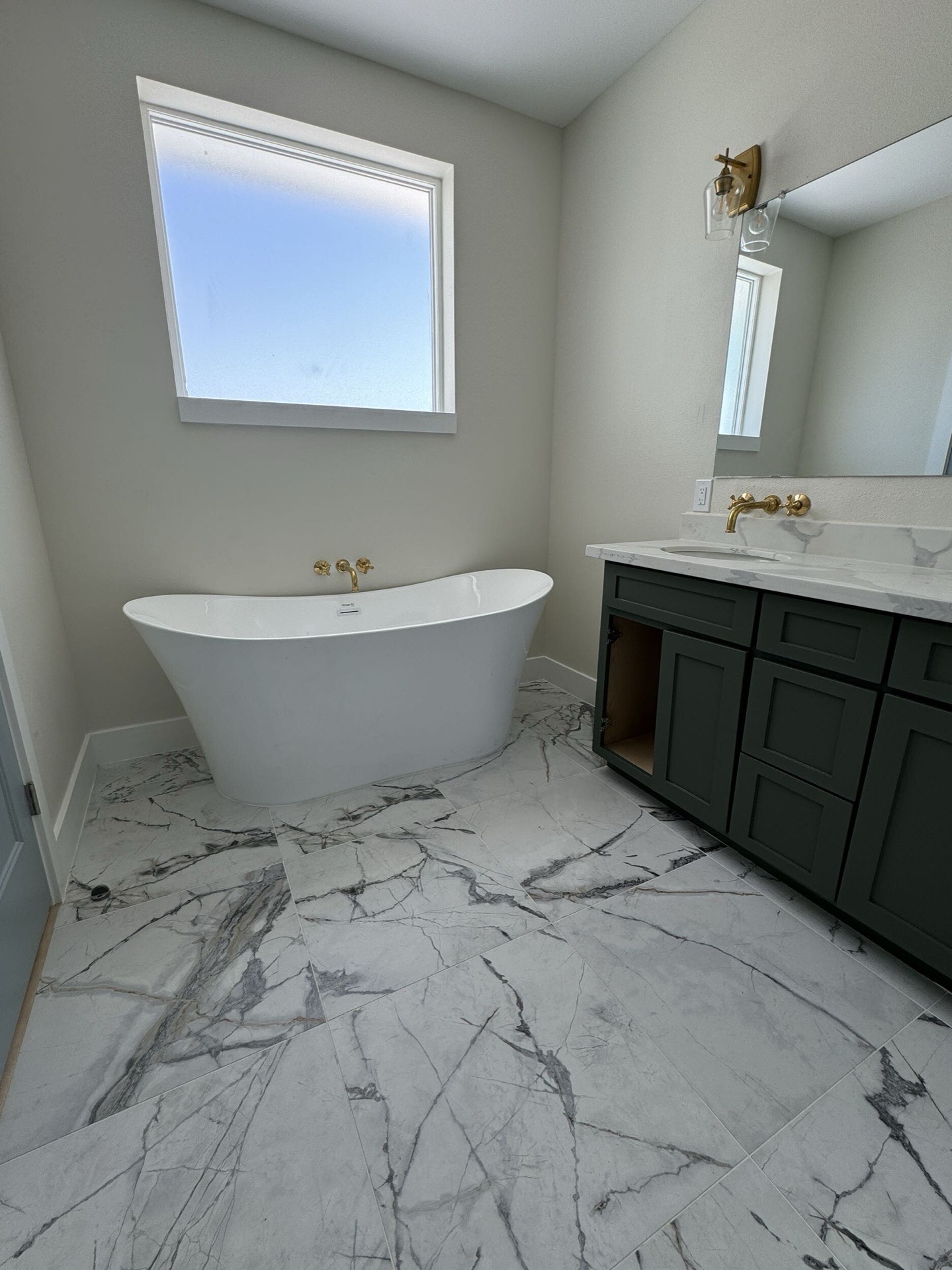 Dark green double vanity detail with white marble top, wall-mounted brass faucets, and framed mirrors in the West Bay master bathroom