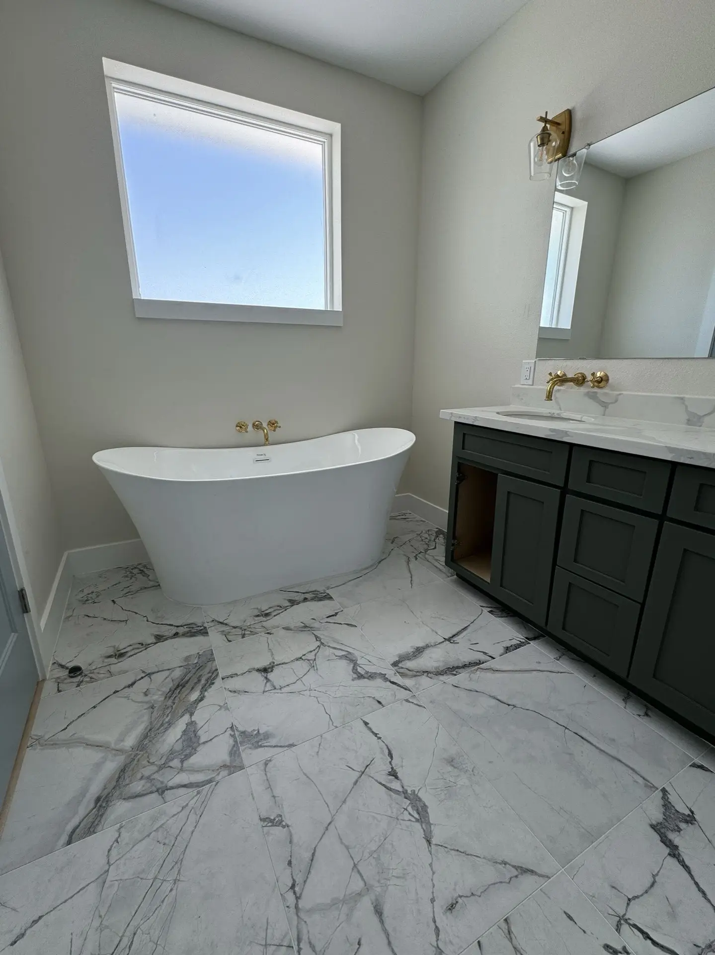 Dark green double vanity detail with white marble top, wall-mounted brass faucets, and framed mirrors in the West Bay master bathroom