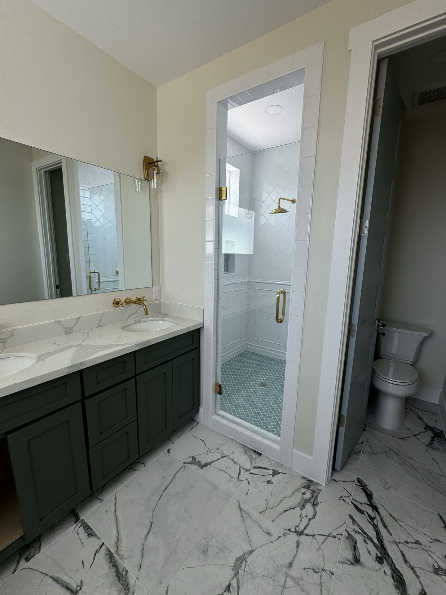 Master bath shower with large-format tile surround, glass enclosure, brass shower fixtures, and built-in niche for toiletries