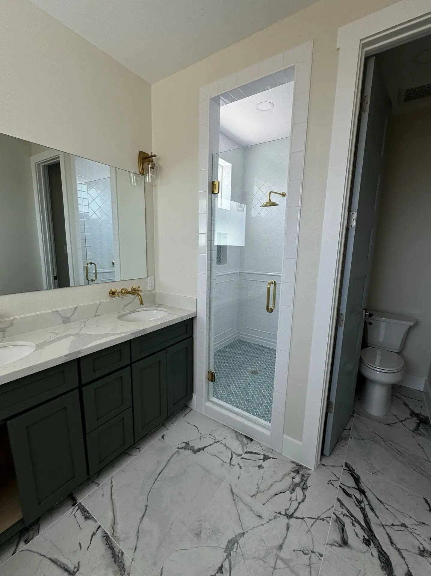 Master bath shower with large-format tile surround, glass enclosure, brass shower fixtures, and built-in niche for toiletries